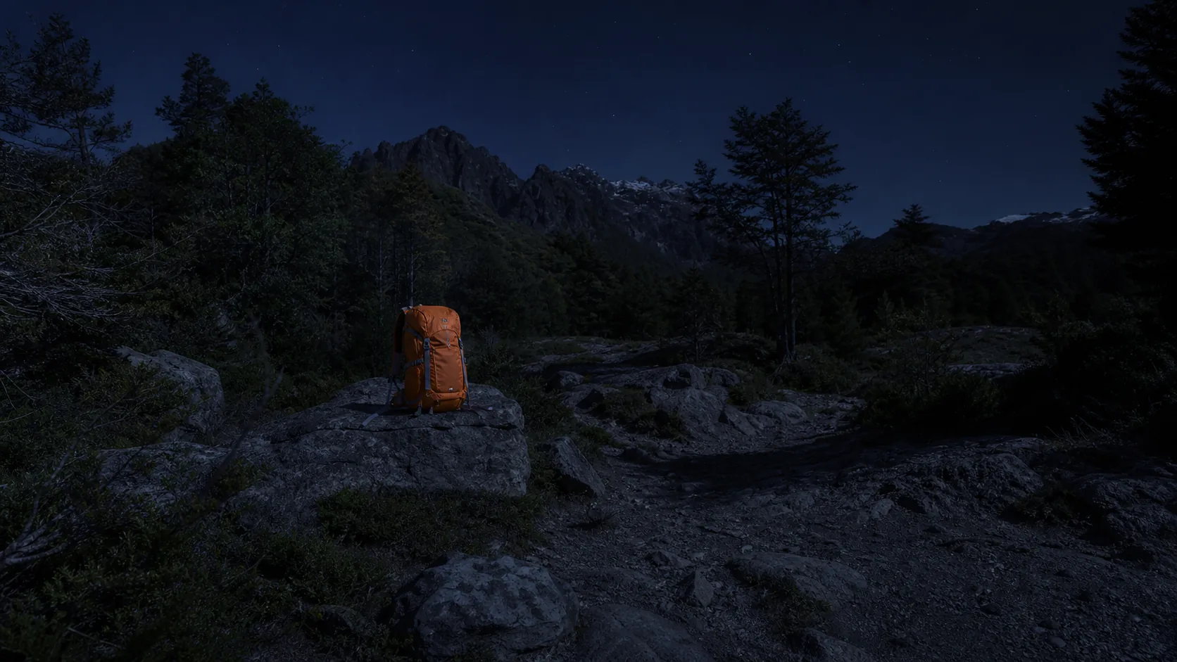 Mochila naranja sobre una roca en un sendero de montaña durante la noche